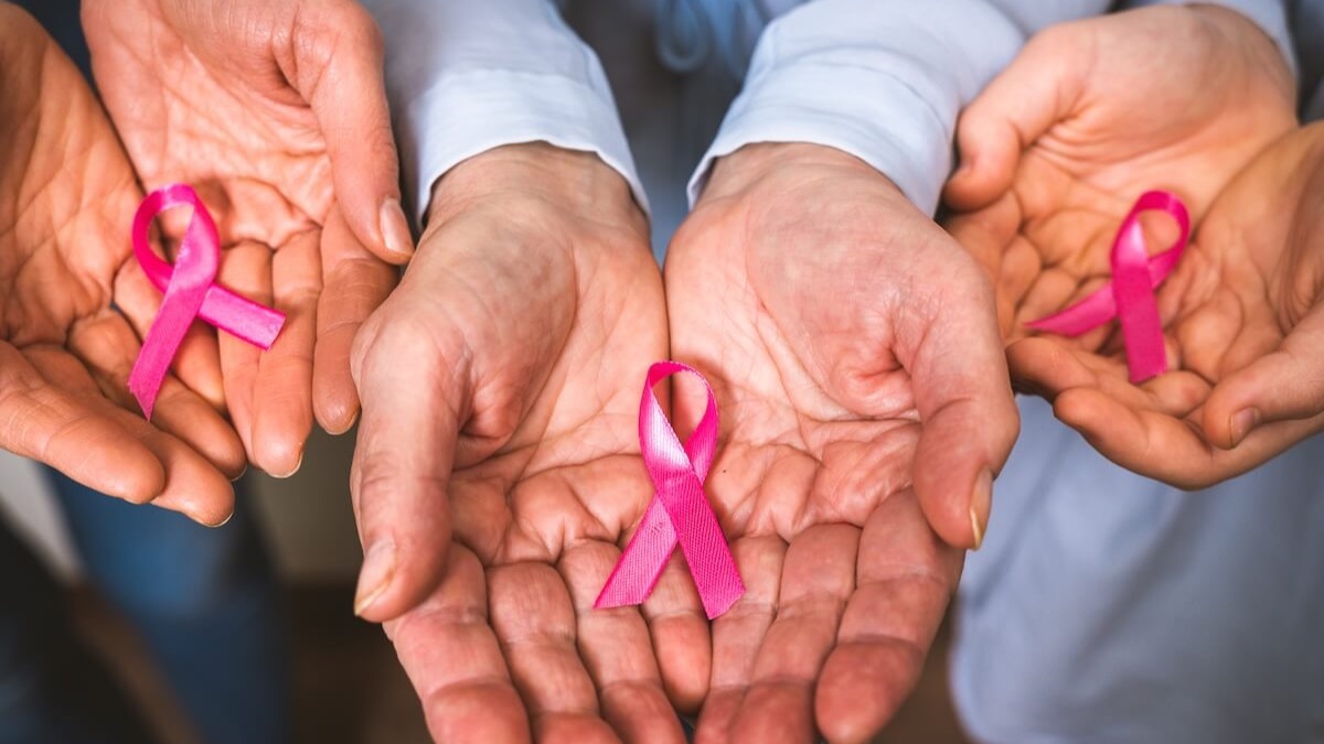 Three pairs of open hands each holding a pink breast cancer awareness ribbon