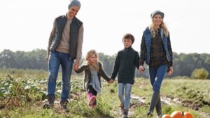 Family holding hands while walking through a farm field with pumpkins on a fall day